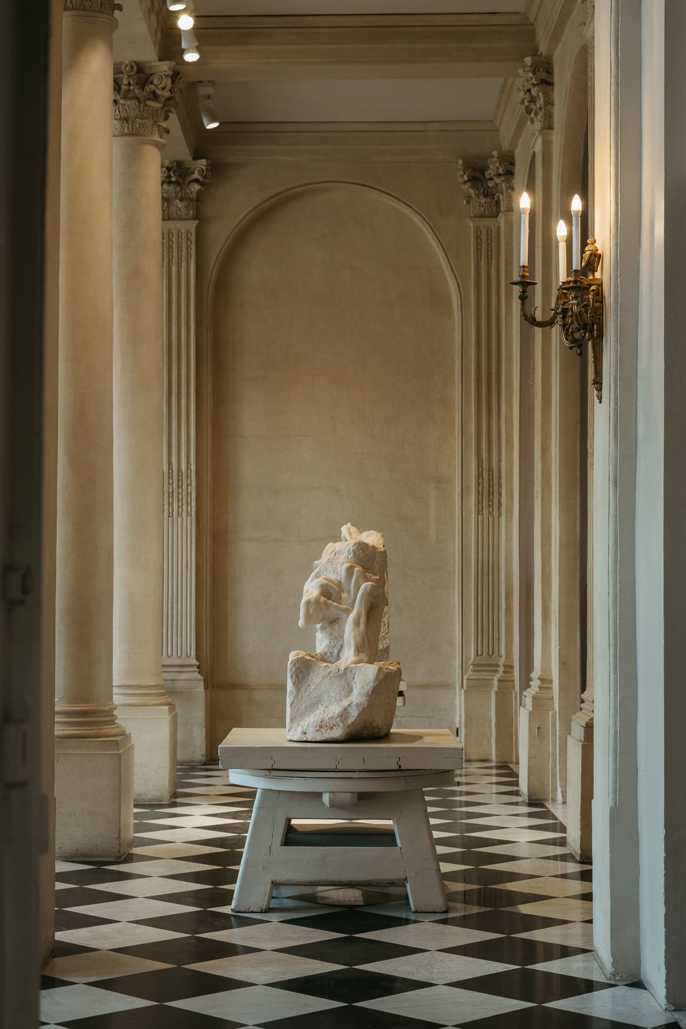 An unfinished sculpture sits on a table on a black and white checkered floor.