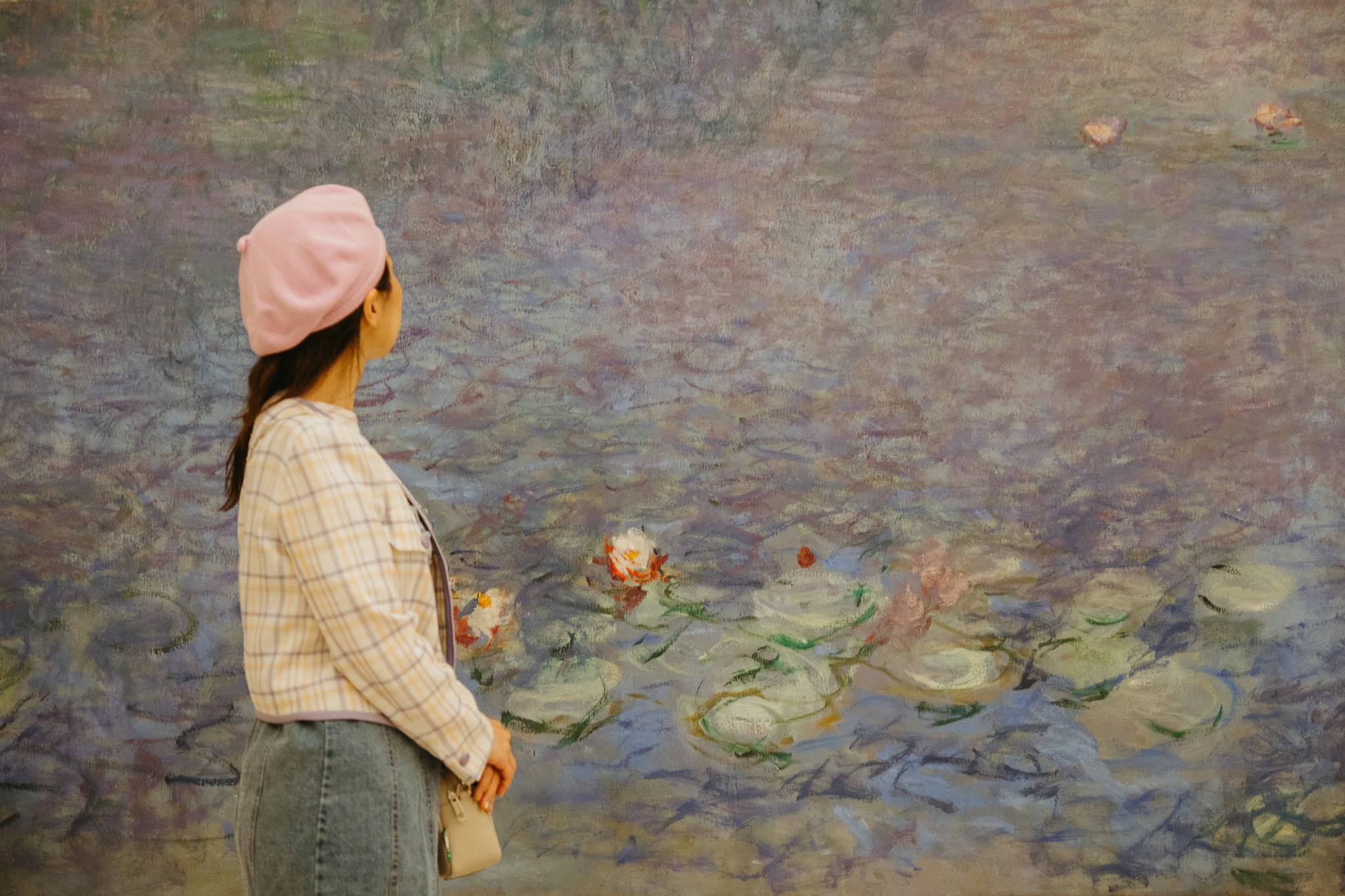 Woman wearing pink beret stands in front of water lilies painting.