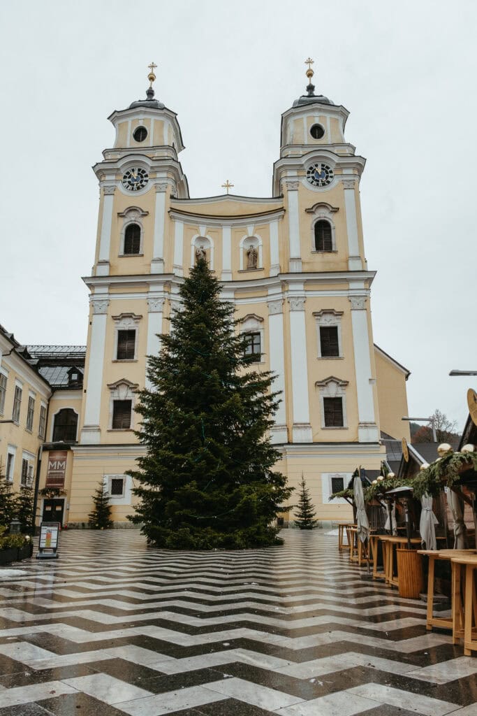 A yellow and white church with a Christmas tree in front of it.