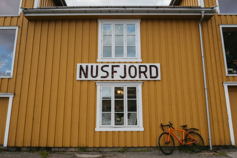 Yellow building that says NUSFJORD with a bike leaning against it.