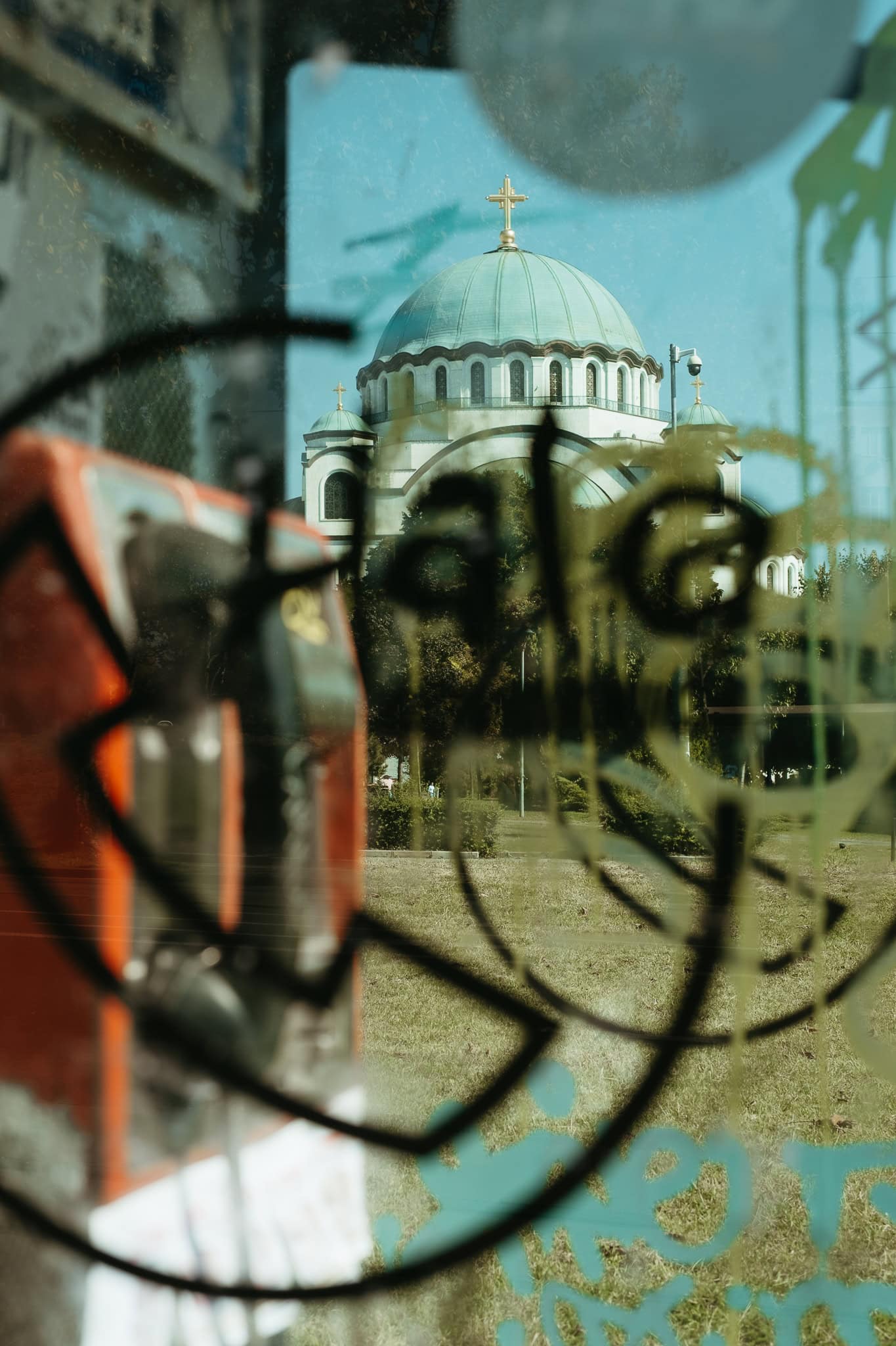 Dome of Saint Sava through the graffitied glass walls of a phone booth.