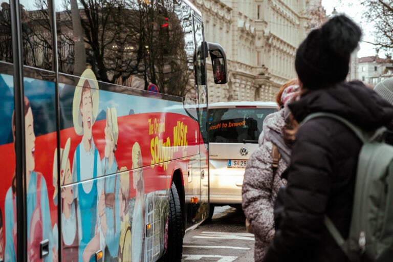 People wait outside a tour bus with images of characters from The Sound of Music.